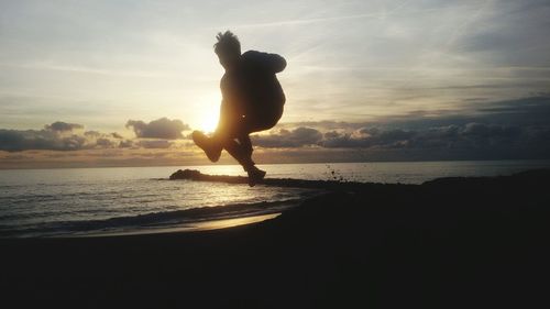 Silhouette boy standing on beach against sky during sunset