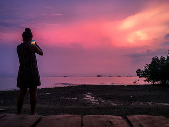 Rear view of silhouette woman standing at beach during sunset
