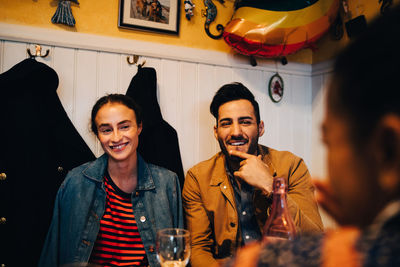 Smiling young man and woman looking at female friend during dinner party at restaurant