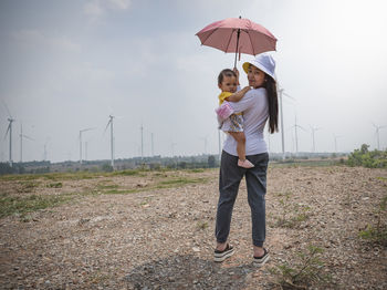 A young mother and her lovely little daughter are at a windmill field.