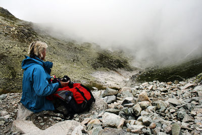 Side view of man sitting on rocks by mountains during winter