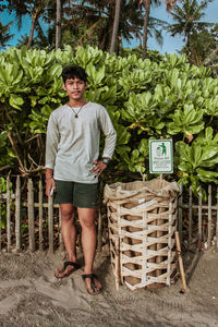 Full length portrait of young man standing against plants