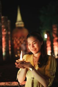 Portrait of young woman holding illuminated while standing at night