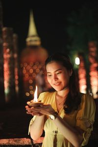 Smiling young woman holding diya while standing in temple