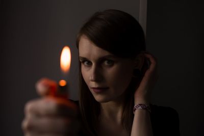 Portrait of young woman holding cigarette against black background