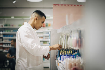 Side view of confident owner arranging medicines on rack in pharmacy store