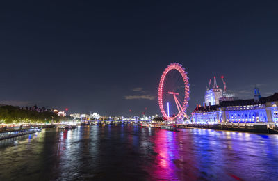 Illuminated ferris wheel by river against sky at night