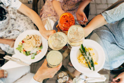 Overhead view of friends having brunch, toasting, saying cheers holding aperol spritz cocktails. 