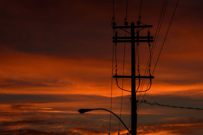 Low angle view of electricity pylon and street light against orange sky