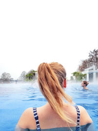 Rear view of woman in swimming pool against clear sky