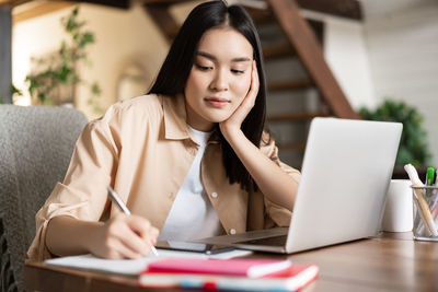 Young woman using laptop while sitting on table