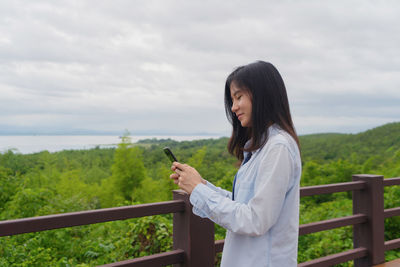 Woman using phone while standing by railing