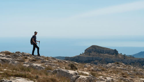 Side view of man standing on rock against sky