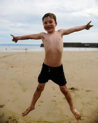 Full length of shirtless boy at beach against sky