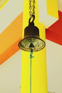 Low angle view of metal hanging against yellow wall