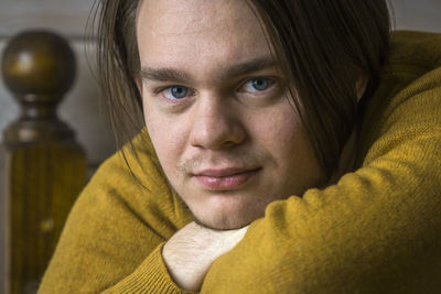 Close-up of young man wearing sweater leaning on wooden railing at home