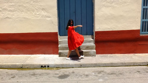 Young woman in red dress dancing on sidewalk