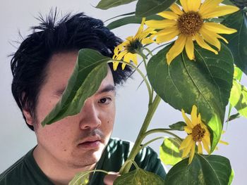 Portrait of young man with sunflower against plants