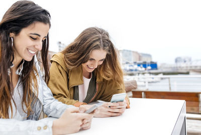 Two happy young women sending messages with their smartphones