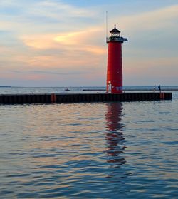 Lighthouse by sea against sky during sunset