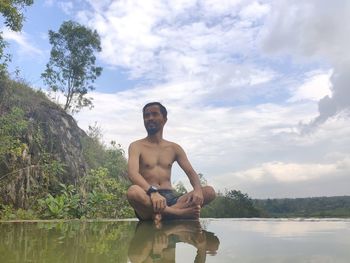 Full length of shirtless man standing by tree against sky