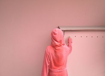 Rear view of woman wearing hooded shirt touching hole on door