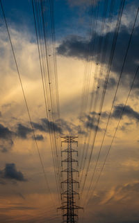 Low angle view of electricity pylon against sky at sunset