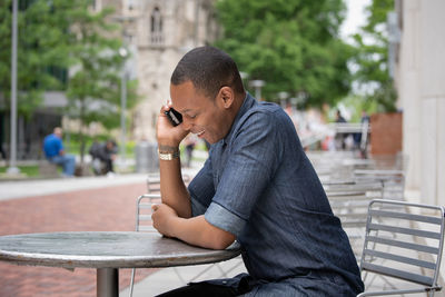 Side view of man using mobile phone while sitting on table