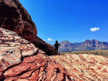 Man standing on rock formation against clear blue sky