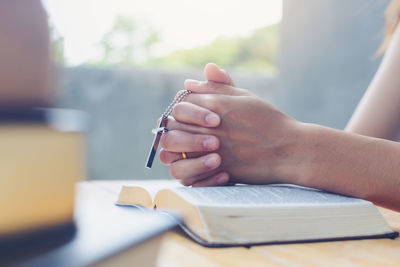 Midsection of woman praying with cross and book on table