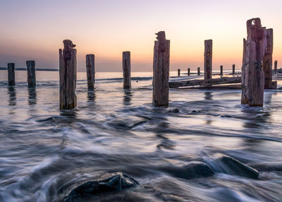 Wooden posts in sea against sky during sunset