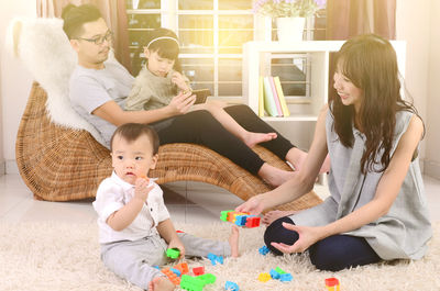 Smiling woman by man and daughter playing with baby boy on carpet at home 