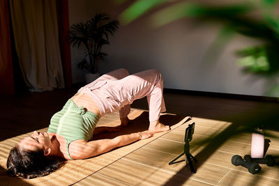 Woman practicing yoga and meditation at home online sitting on yoga mat