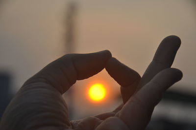 Close-up of hand holding sun during sunset