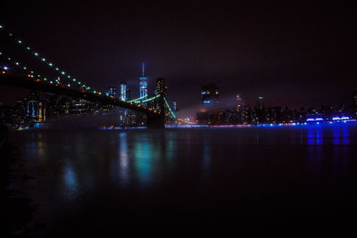 Illuminated modern buildings by river against sky at night