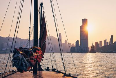 Sailboat in sea against cityscape during sunset