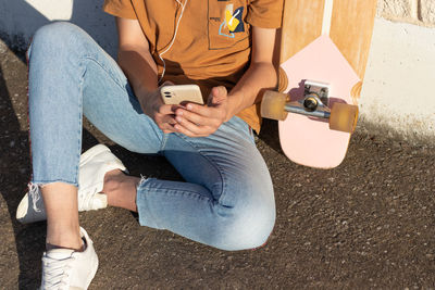 Unrecognizable young man sitting on the city floor listening to music messages and a skateboard 