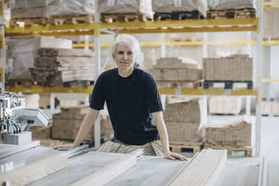 Portrait of mature female worker standing by wooden planks at table in industry