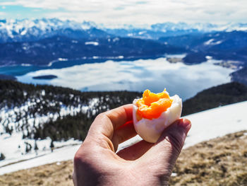 Close-up of hand having boiled egg against lake and snowcapped mountains