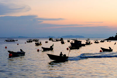 Fishing boats on sea against sky during sunset