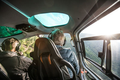 Rear view of helicopter pilot flying low through forested mountains.