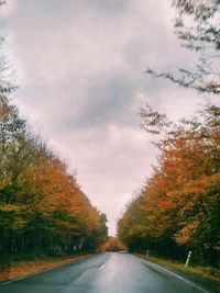 Empty road amidst trees against sky during autumn
