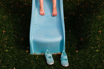 Barefoot child on blue slide with shoes on ground