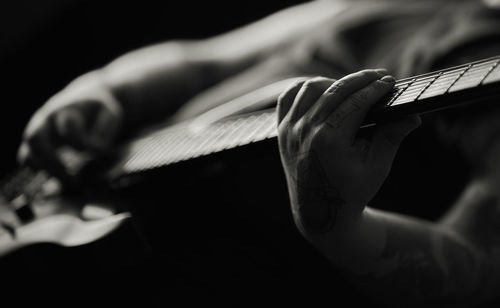 Midsection of man playing guitar against black background