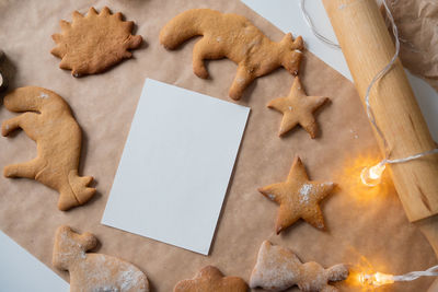 A frame with a white sheet of ginger cookies of different shapes on parchment, a rolling pin 