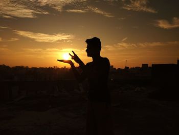 Optical illusion of silhouette man striking sun against sky during sunset