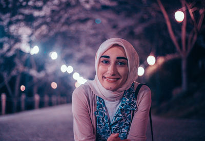 Portrait of smiling young woman in illuminated city at night