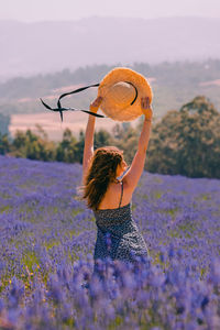 Portrait of young woman with arms raised standing against sky