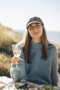 Portrait of beautiful young woman wearing cap while holding wineglass at dinner party