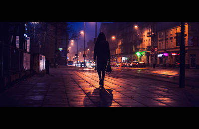 Rear view of silhouette man walking on illuminated street at night